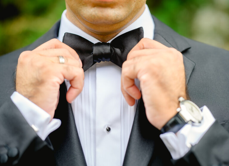 Groom adjusting his tie before wedding ceremony in formal attire.